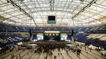 Wide shot of a crowded concert in a large indoor arena with a prominent stage.