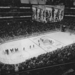 Black and white overhead shot of a thrilling ice hockey game with a full audience in an indoor arena.