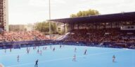 Field hockey match in a vibrant stadium during Paris 2024 event, showcasing athlete action and large crowd.