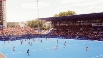 Field hockey match in a vibrant stadium during Paris 2024 event, showcasing athlete action and large crowd.