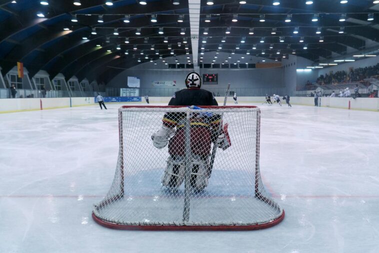 Dynamic scene of a thrilling ice hockey match with goalie ready in front of the goal.