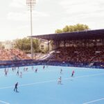 Field hockey match in a vibrant stadium during Paris 2024 event, showcasing athlete action and large crowd.