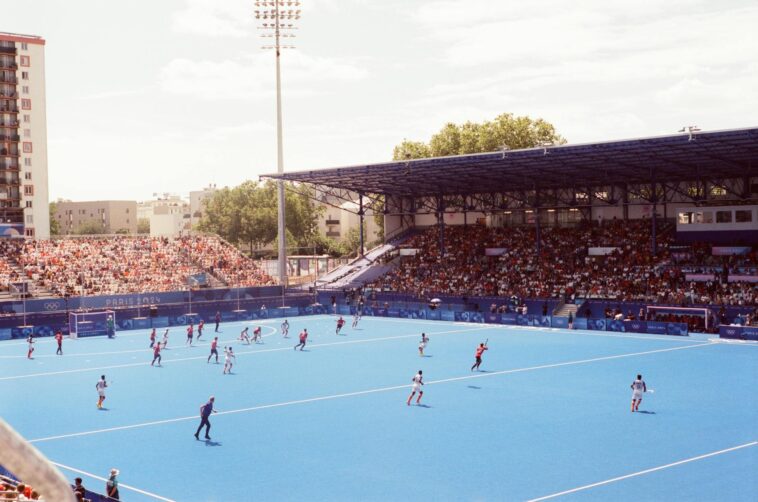 Field hockey match in a vibrant stadium during Paris 2024 event, showcasing athlete action and large crowd.