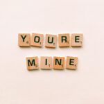 Romantic message You're Mine created with wooden Scrabble tiles on a pink background.