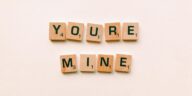 Romantic message You're Mine created with wooden Scrabble tiles on a pink background.