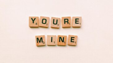 Romantic message You're Mine created with wooden Scrabble tiles on a pink background.