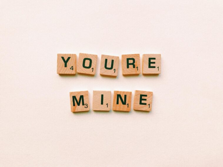 Romantic message You're Mine created with wooden Scrabble tiles on a pink background.