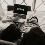 A couple relaxing together, watching Netflix on a laptop in a cozy bedroom setting.