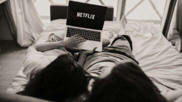 A couple relaxing together, watching Netflix on a laptop in a cozy bedroom setting.