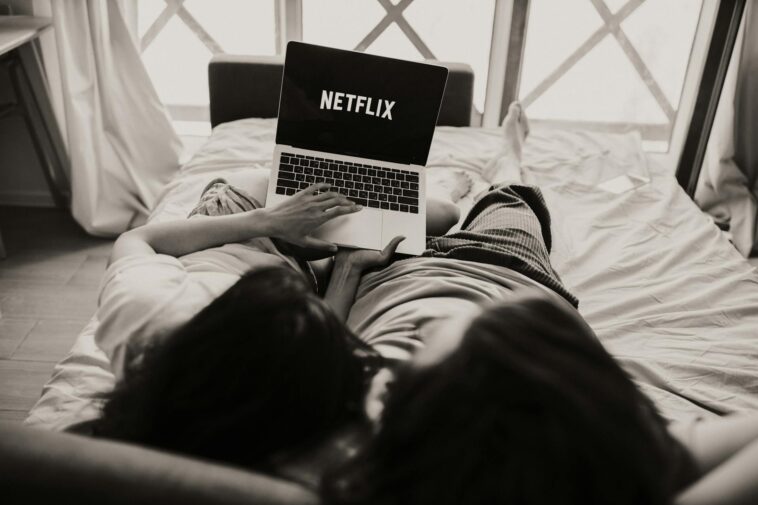 A couple relaxing together, watching Netflix on a laptop in a cozy bedroom setting.