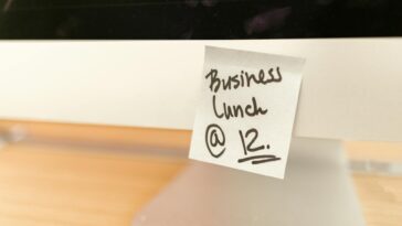 Close-up of a sticky note reminder for a business lunch at 12 o'clock on a computer monitor.