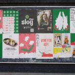 Colorful urban bulletin board with various artistic posters in multiple languages.