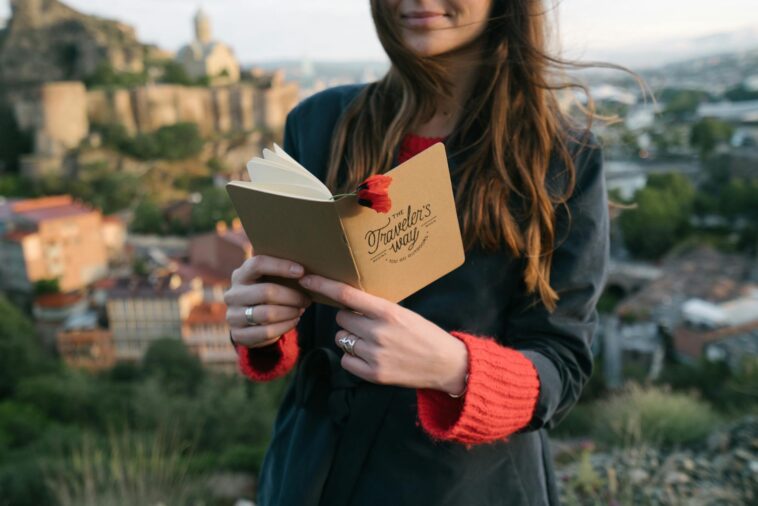 Young woman with a journal enjoys a scenic view from a hilltop.
