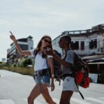 Two women crossing a busy street, exploring a vibrant city while wearing backpacks, capturing the essence of urban travel.