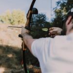 A man aiming a recurve bow during archery practice in a natural setting.