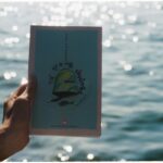 A hand holds a book against a backdrop of sparkling water, creating a calming scene.