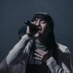 A woman passionately singing into a microphone during a live performance indoors.