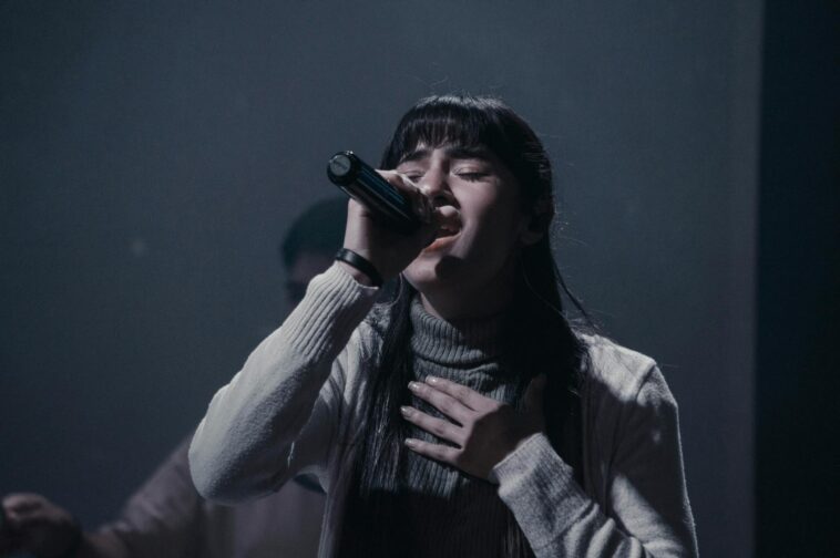 A woman passionately singing into a microphone during a live performance indoors.