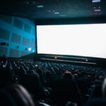A crowded cinema audience seated in a theater watching a movie on a large screen.