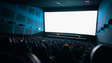 A crowded cinema audience seated in a theater watching a movie on a large screen.