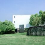 A modern museum building with a stone tablet, surrounded by lush greenery and clear sky.