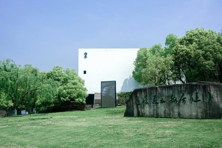 A modern museum building with a stone tablet, surrounded by lush greenery and clear sky.