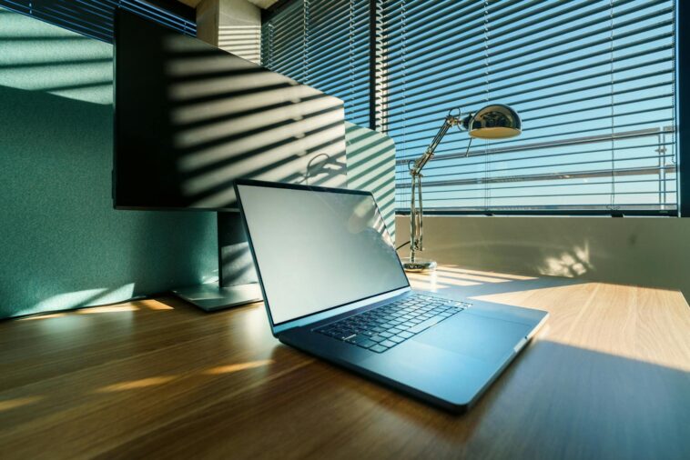 A clean, sunlit office desk with a modern laptop and monitor, perfect for business or corporate settings.