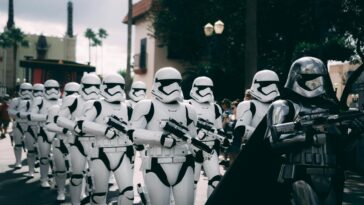 Group of stormtroopers marching outdoors during a cosplay event at a theme park.