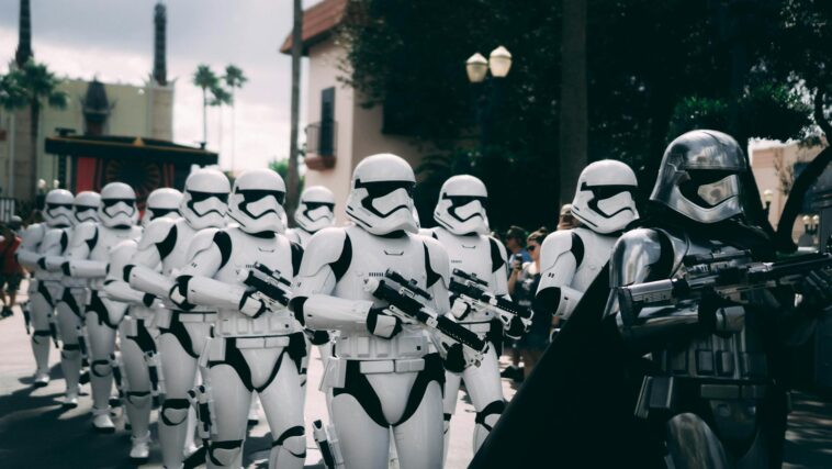 Group of stormtroopers marching outdoors during a cosplay event at a theme park.