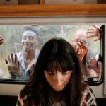 A woman sits unaware while terrifying zombies threaten through the window.