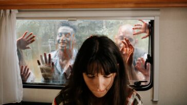 A woman sits unaware while terrifying zombies threaten through the window.