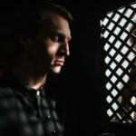 A priest listens to a penitent in a dimly lit confessional, embodying themes of faith and repentance.