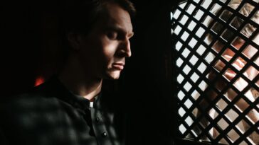 A priest listens to a penitent in a dimly lit confessional, embodying themes of faith and repentance.