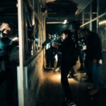 A cinematic scene capturing actors filming an intense action sequence in a dimly lit warehouse.