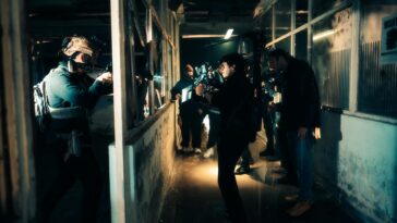 A cinematic scene capturing actors filming an intense action sequence in a dimly lit warehouse.