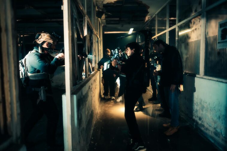 A cinematic scene capturing actors filming an intense action sequence in a dimly lit warehouse.