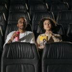 A couple sits in a cinema, enjoying popcorn while watching a movie.