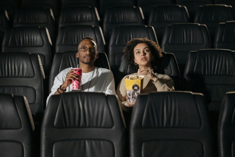 A couple sits in a cinema, enjoying popcorn while watching a movie.