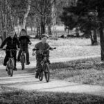 Black and white photo of three kids cycling on a path through a park.