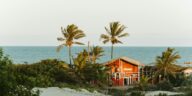 Scenic view of a rustic beach house in Itaúnas, surrounded by palms and sandy shores.