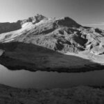 Captivating black and white photograph of a mountain range with a winding river in the foreground.