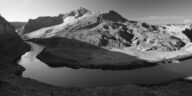 Captivating black and white photograph of a mountain range with a winding river in the foreground.