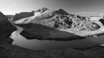 Captivating black and white photograph of a mountain range with a winding river in the foreground.