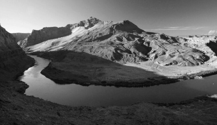 Captivating black and white photograph of a mountain range with a winding river in the foreground.