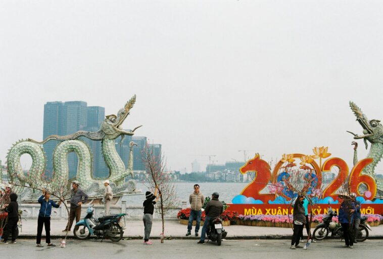 People preparing for Lunar New Year 2026 by a dragon statue along a lakeside.