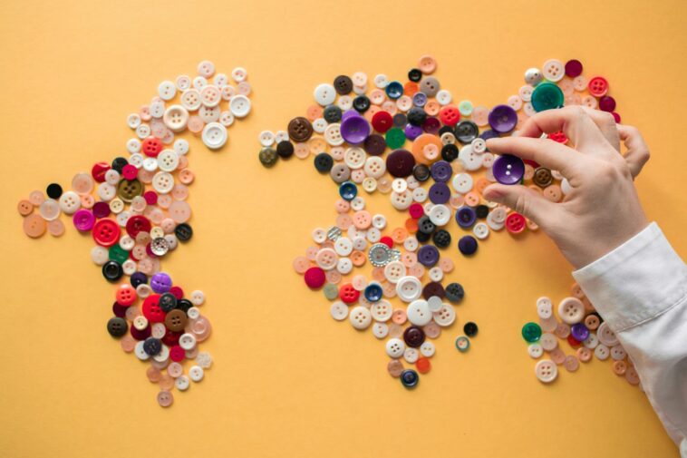 Hand arranging colorful buttons to form a world map on a vibrant yellow background.