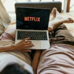 A couple lying comfortably in bed watching Netflix on a laptop, enjoying leisure time together indoors.