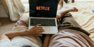 A couple lying comfortably in bed watching Netflix on a laptop, enjoying leisure time together indoors.