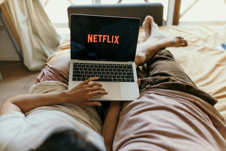A couple lying comfortably in bed watching Netflix on a laptop, enjoying leisure time together indoors.