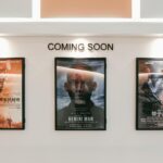 Framed posters of upcoming movies in a cinema hallway under 'Coming Soon' sign.